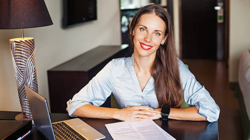 Beautiful business woman in casual dress sitting at a table with laptop looking at camera and smiling